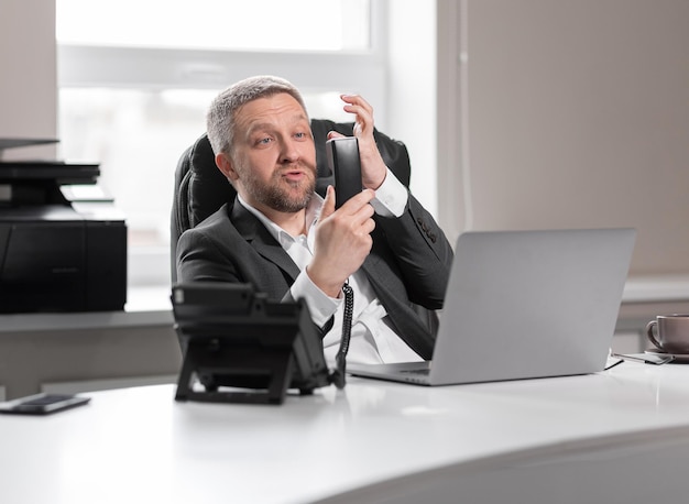 Hombre adulto guapo con traje gris sostiene un teléfono y se enoja