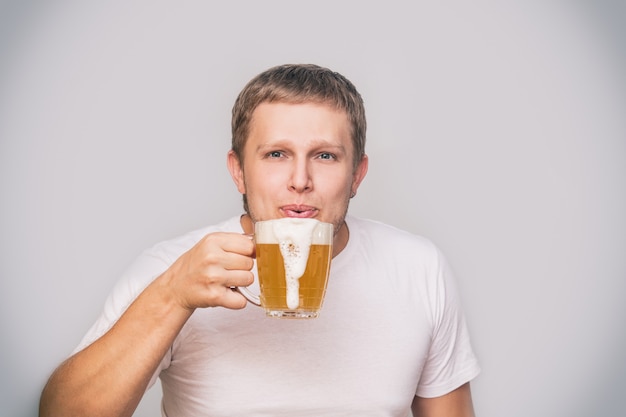 Hombre adulto joven de apariencia europea con una jarra de cerveza en una camiseta blanca sobre un fondo aislado en el estudio