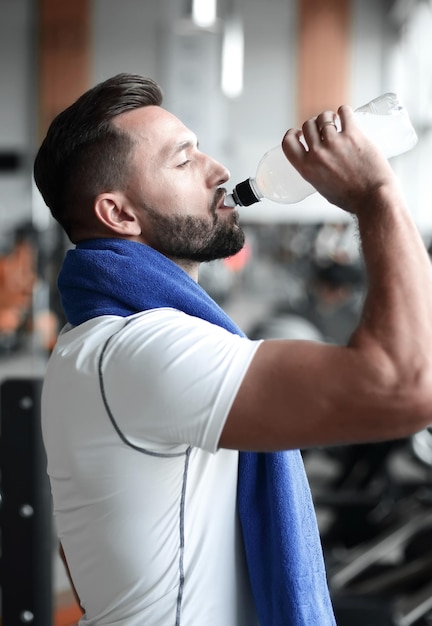Hombre adulto joven bebiendo una botella de agua en la caminadora en el gimnasio