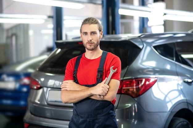 Hombre adulto joven confiado en uniforme de trabajo de pie cerca de coches en la sala de exposición de coches