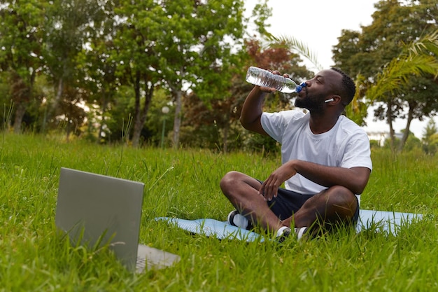 Hombre adulto joven feliz descansando en el parque después de entrenar en línea entrenamientos al aire libre