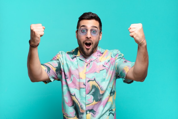 Hombre adulto joven guapo celebrando un éxito increíble como un ganador, mirando emocionado y feliz diciendo ¡tómate eso!