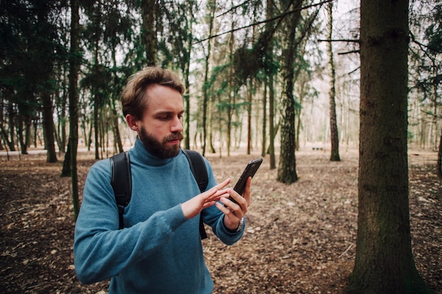 Hombre adulto joven hablando por teléfono de pie sobre el bosque estresado con la mano en la cabeza