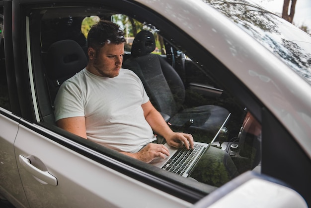Hombre adulto joven que trabaja en el coche en la computadora portátil