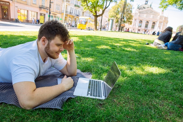 Hombre adulto joven que trabaja en la computadora portátil en el parque de la ciudad en el día de verano