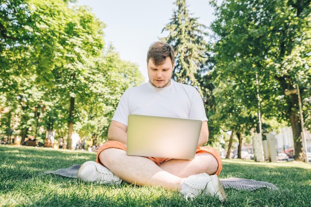 Hombre adulto joven que trabaja en la computadora portátil en el parque de la ciudad en el día de verano