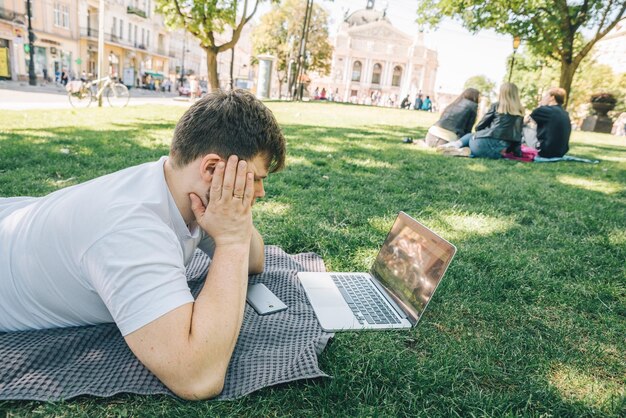 Foto hombre adulto joven que trabaja en la computadora portátil en el parque de la ciudad en el día de verano