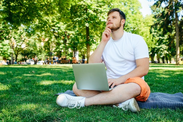 Hombre adulto joven que trabaja en la computadora portátil en el parque de la ciudad en el día de verano