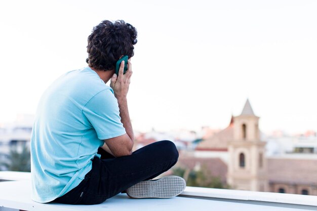 Hombre adulto joven sentado al aire libre y usando su teléfono inteligente