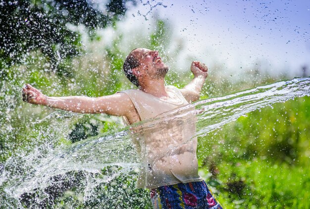 Hombre adulto del lado del país que disfruta del flujo agudo del agua durante los tiempos de calor del verano.