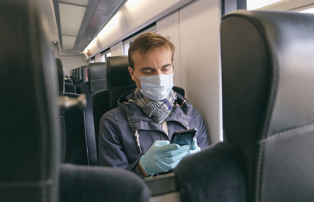 Hombre adulto con máscara protectora médica y guantes sentado dentro de un tren vacío