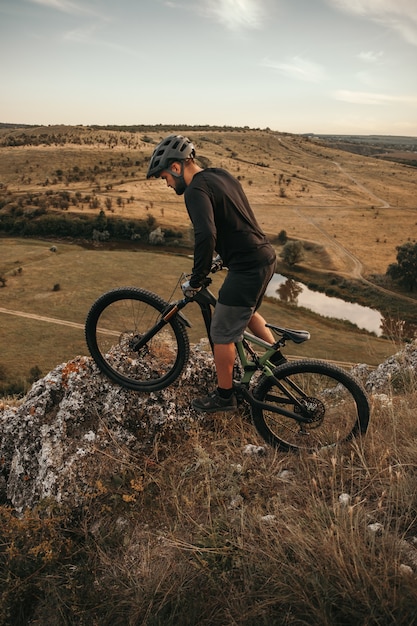 Hombre adulto montando bicicleta en terrenos montañosos al atardecer