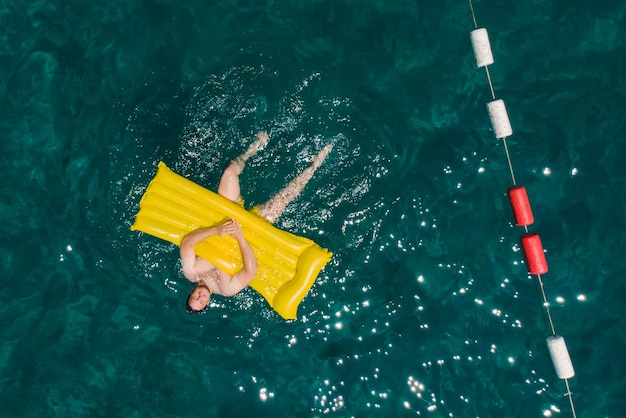 hombre adulto nadando en un colchón inflable amarillo en las montañas del mar azul en el fondo