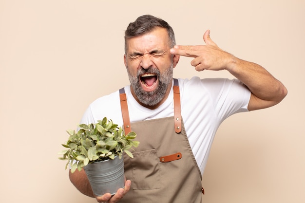 Hombre adulto que parece infeliz y estresado, gesto de suicidio haciendo un signo de pistola con la mano, apuntando a la cabeza