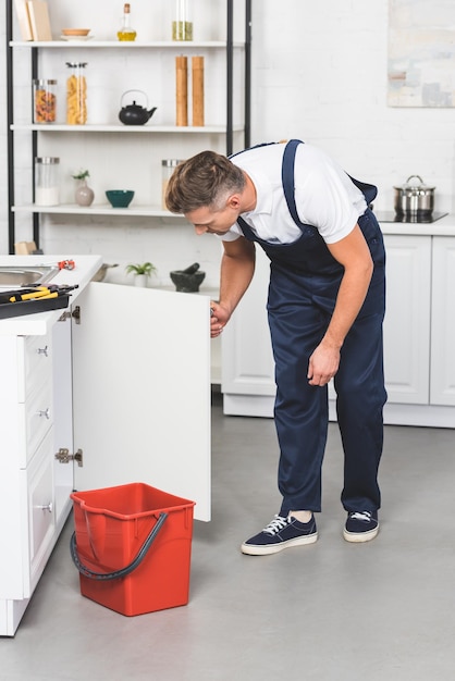 Hombre adulto en ropa de trabajo reparando fregadero de cocina