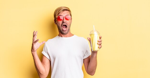 Hombre adulto rubio gritando con las manos en el aire con un batido