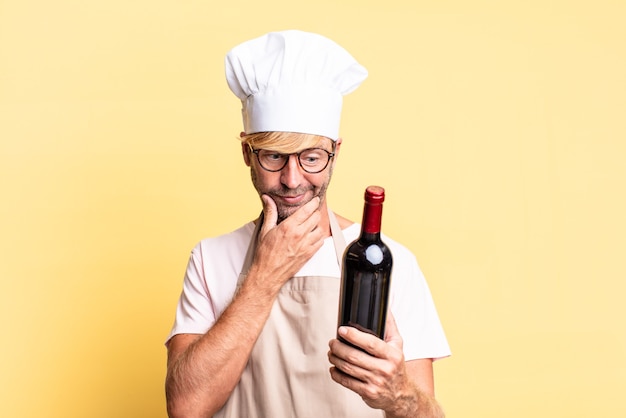 Hombre adulto rubio guapo chef sosteniendo una botella de vino