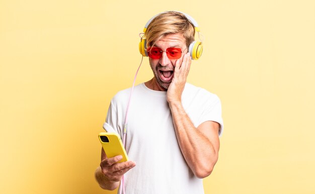 Hombre adulto rubio que se siente feliz, emocionado y sorprendido con auriculares