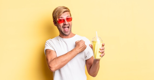 Hombre adulto rubio que se siente feliz y enfrenta un desafío o celebra con un batido