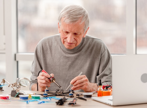 Hombre adulto sentado junto a la mesa y soldar cables durante el proceso de reparación de quadcopter