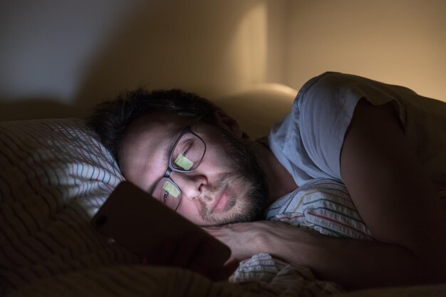 Foto hombre adulto somnoliento con gafas navegando en la web antes de soñar con adicción a las redes sociales
