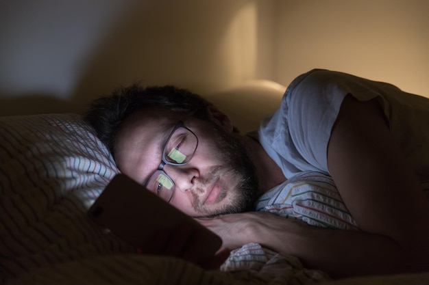 Hombre adulto somnoliento con gafas navegando en la web antes de soñar Trastorno del sueño