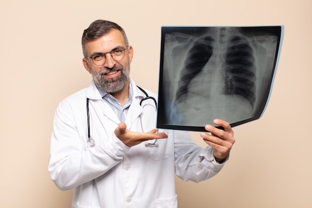 Hombre adulto sonriendo alegremente, sintiéndose feliz y mostrando un concepto en el espacio de la copia con la palma de la mano