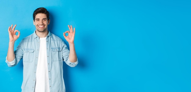 Hombre adulto sonriente confiado que muestra señales de ok y parece complacido como algo que se opone a blu