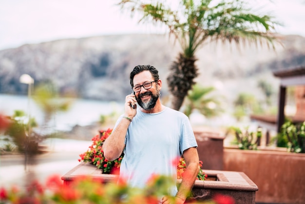 Hombre adulto sonriente hablando por teléfono al aire libre en casa