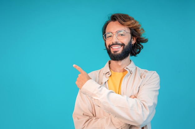 Hombre adulto sonriente introduce el producto señalando con el dedo contra un fondo azul con espacio de copia