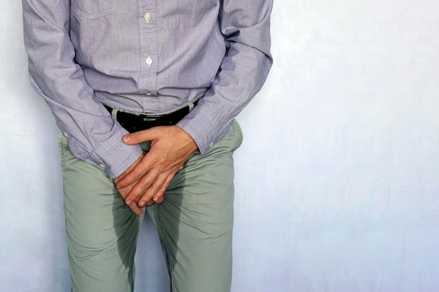 El hombre adulto sostiene las manos en el área de la ingle y los pantalones mojados por la orina Concepto de incontinencia urinaria Persona mojada Fondo azul Problema de salud Concepto médico espacio de copia