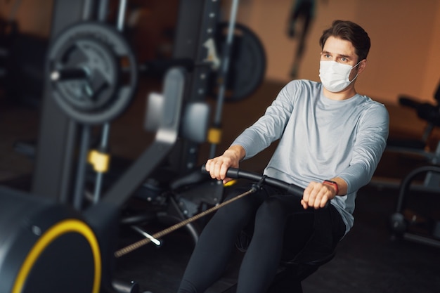 Hombre adulto trabajando en un gimnasio en máscara debido a covid-19