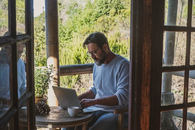 Hombre adulto usa ordenador portátil sentado al aire libre en casa en la actividad de trabajo en línea de trabajo inteligente de oficina alternativa. La gente moderna disfruta de la tecnología de conexión inalámbrica para trabajar de forma remota