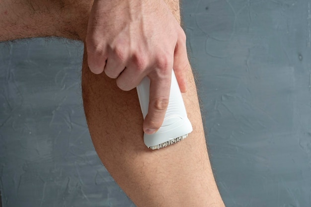 Un hombre se afeita el vello de las piernas con una depiladora eléctrica blanca. la belleza de los hombres.