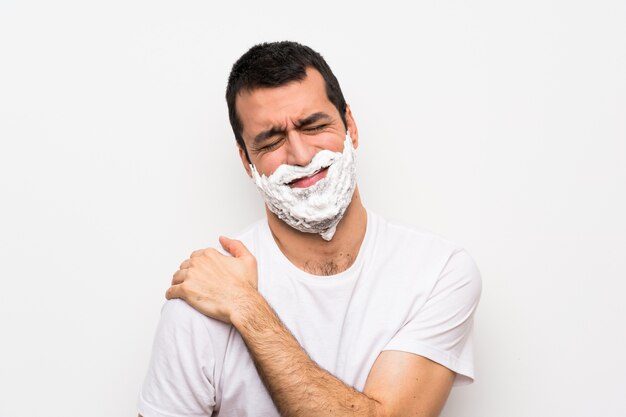 Hombre afeitándose la barba sobre una pared blanca aislada que sufre de dolor en el hombro por haber hecho un esfuerzo