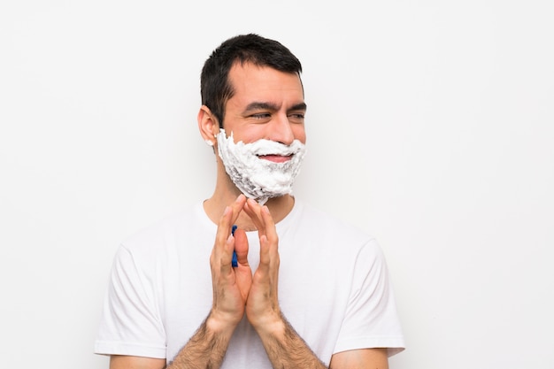 Foto hombre afeitándose la barba sobre una pared blanca aislada, tramando algo