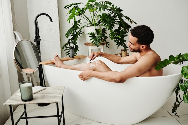 Hombre afeitándose las piernas en el baño.