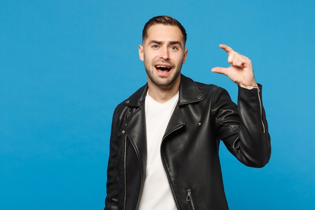 Hombre sin afeitar joven elegante hermoso en camiseta blanca de la chaqueta de cuero negra que mira la cámara aislada en el retrato azul del estudio del fondo de la pared. Concepto de estilo de vida de emociones sinceras de personas. Simulacros de espacio de copia