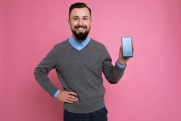 Hombre sin afeitar de pared joven fresco feliz guapo positivo con barba vistiendo elegante suéter gris y