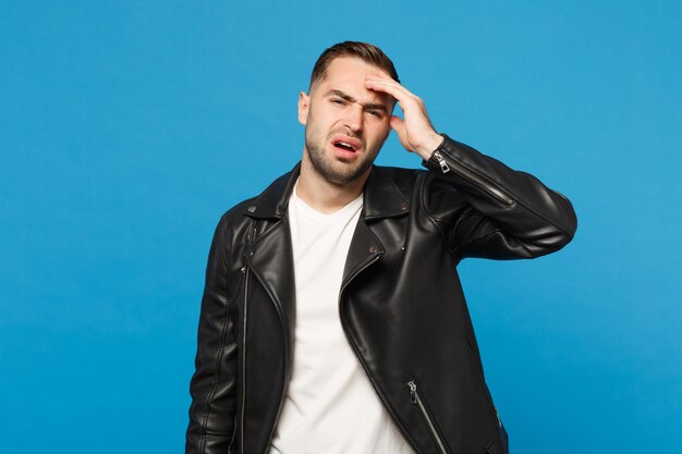 Hombre sin afeitar preocupado frustrado triste joven en camiseta blanca de la chaqueta negra que mira la cámara aislada en el retrato azul del estudio del fondo de la pared. Concepto de estilo de vida de emociones sinceras de personas. Simulacros de espacio de copia.