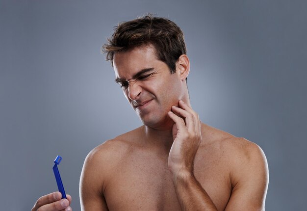 Hombre afeitarse y barba o afeitarse en el estudio para la depilación error inflamación o fondo gris Hombre herramienta de persona y inclinarse o accidente infeliz para el mantenimiento del bienestar dolor o maqueta