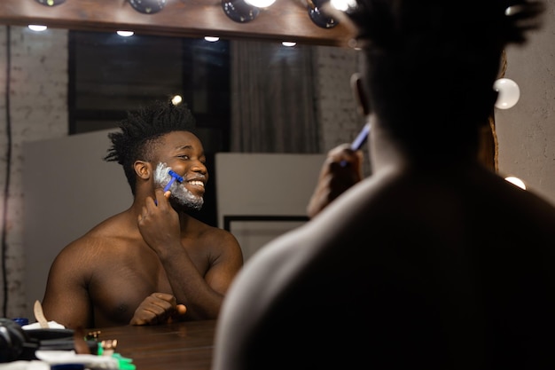 hombre africano adulto afeitándose en el interior en el espejo