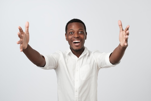 Hombre africano alegre con camisa blanca tirando de las manos hacia la cámara queriendo abrazar