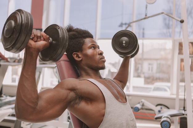 Hombre africano atlético ejercitarse con pesas en el gimnasio