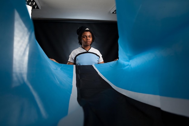 Hombre africano de Botswana con una bandera sonriendo en un estudio fotográfico contra un fondo oscuro