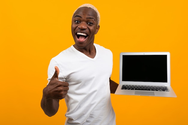 Hombre africano con cabello blanco sonriendo sosteniendo la pantalla del portátil hacia adelante con maqueta sobre fondo amarillo