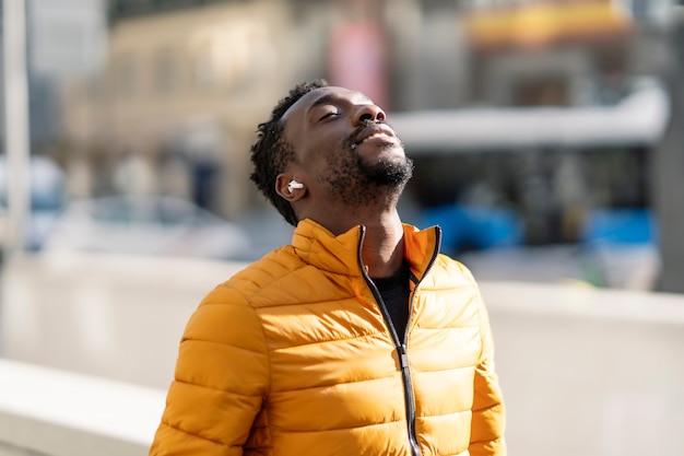 Hombre africano escuchando música y respirando aire fresco al aire libre de pie en la ciudad