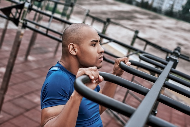 Un hombre africano está tirando hacia arriba en el gimnasio al aire libre vista lateral de cerca