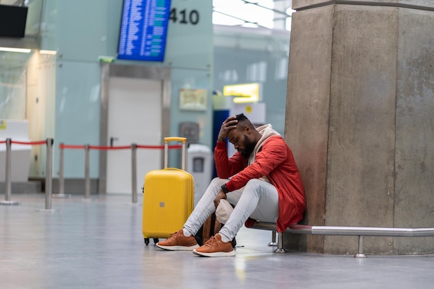 Hombre africano exhausto en una larga conexión nocturna en el aeropuerto esperando un avión sentado en la terminal