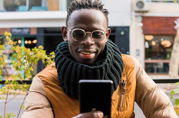 Hombre africano feliz al aire libre sonríe y revisa las notificaciones en la vista frontal de su teléfono